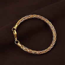 Gold and silver braided bracelet on a brown fabric background with 'Geezenca' branding.