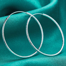 Silver hoop earrings on a teal fabric background.