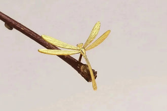Gold dragonfly pendant on a branch with 'GEEZENCA' branding.
