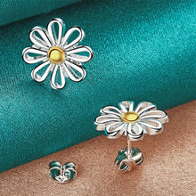 Silver flower-shaped earrings with a gold center on a teal fabric background