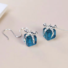 Blue gift box earrings with silver ribbons on a beige background, branded 'GEEZENCA'.