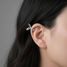 Silver leaf-shaped earring worn by a person with dark hair.