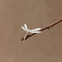 Silver dragonfly earring on a branch with a brown background and 'GEEZENCA' branding.