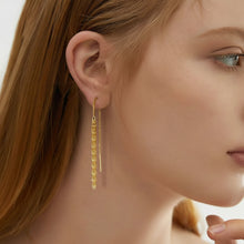 A close-up of a woman's ear and side profile wearing a delicate gold dangle earring with small faceted beads. The brand logo 'Orisa Jewelry' is visible in the top-left corner.