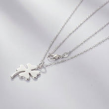 Silver four-leaf clover necklace on a light gray background with teal wooden planks.