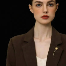 Woman wearing a brown blazer with a gold brooch against a black background.
