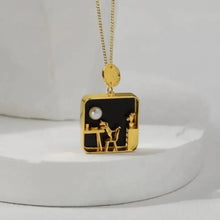 Gold necklace with a black pendant featuring a pearl and two animals on a white background.
