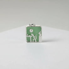 Silver pendant with green background and 'GEEZENCA' branding on a white surface