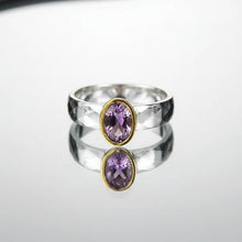 Silver ring with a pink gemstone on a gray background, featuring the brand 