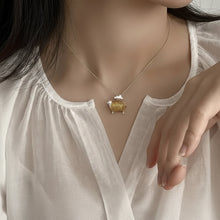 Woman wearing a necklace with a turtle pendant, branded 'GEEZENCA'.