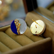 Gold and blue earring on a beige cushion with 'GEEZENCA' branding.