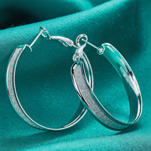 Silver hoop earrings on a teal fabric background with 'Doteffil' branding.