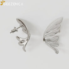 Silver wing-shaped earrings on a light gray background with 'GEEZENCA' branding.