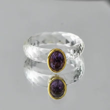 Clear crystal ring with purple gemstones and gold accents on a gray background, featuring the brand 