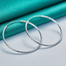 Silver hoop earrings on a light blue fabric background with 'Doteefil' branding.