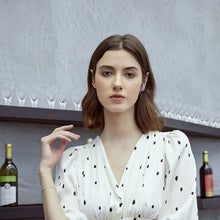 Woman in a white polka dot dress with wine bottles and glasses in the background, featuring the brand 'GEEZENCA'.