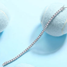 Silver bracelet with clear stones on a light blue background, featuring a brand logo in the corner.

